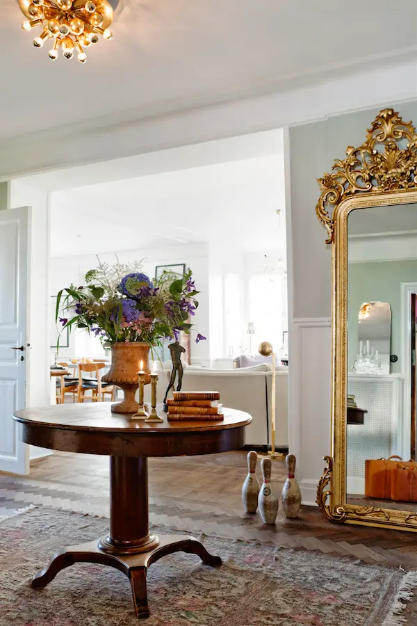 Hall med förgylld spegel, runt pelarbord och blommor, våningen Dusty Deco