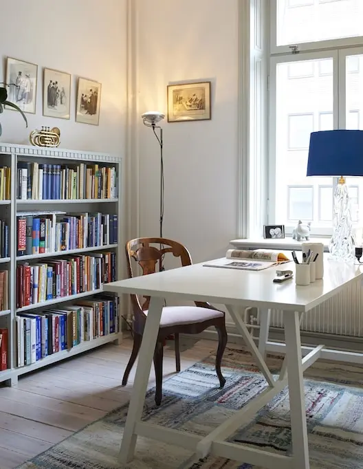 Arbetsrum med bokhyllor, vitt skrivbord och blå bordslampa, våning på Östermalm