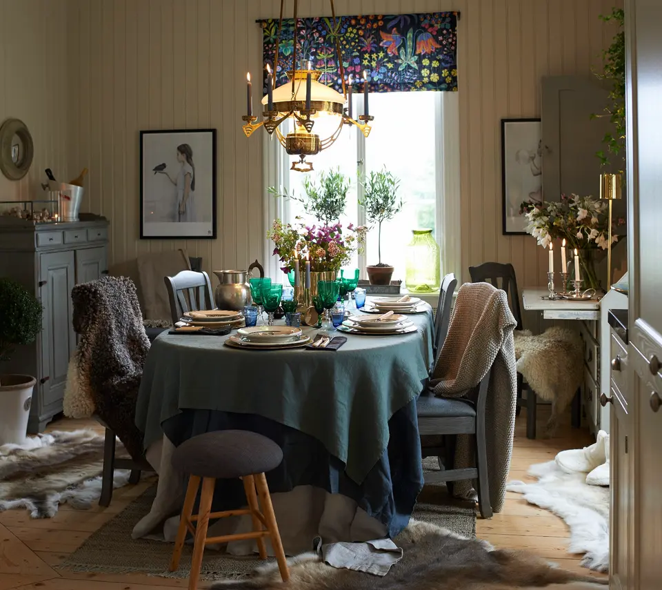 Matplats med dukat runt bord, mässingskrona och blommig gardinkappa, lantkök i skärgården