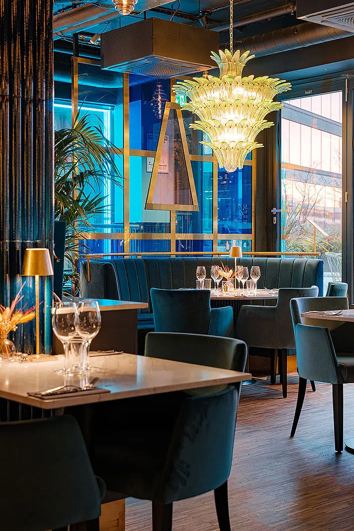 Glasljuskrona över bord i matsalen och blått ljus i fönstren, Restaurang Pava, Stockholm
