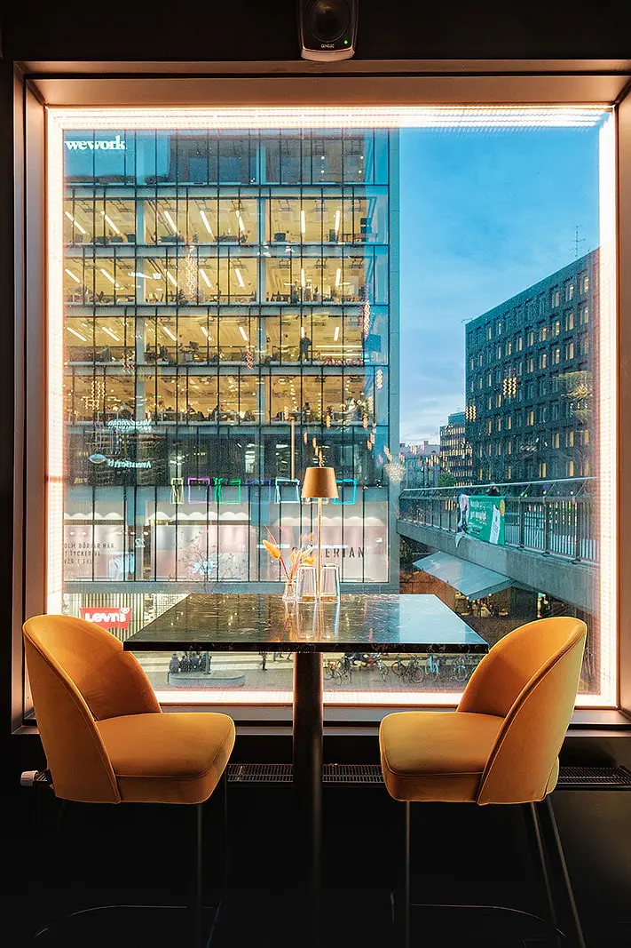 Bord för två med orange stolar vid ett stort fönster mot stan, Restaurang Pava, Stockholm
